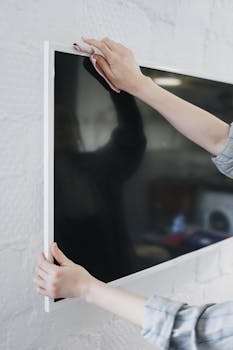 Close-up of a woman's hands wiping a modern flat-screen TV for housework clarity.